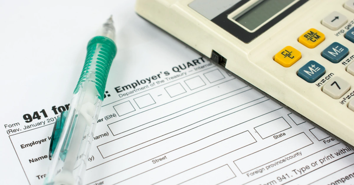 Close-up of IRS Form 941 for employer’s quarterly tax return with a calculator and pen on top.