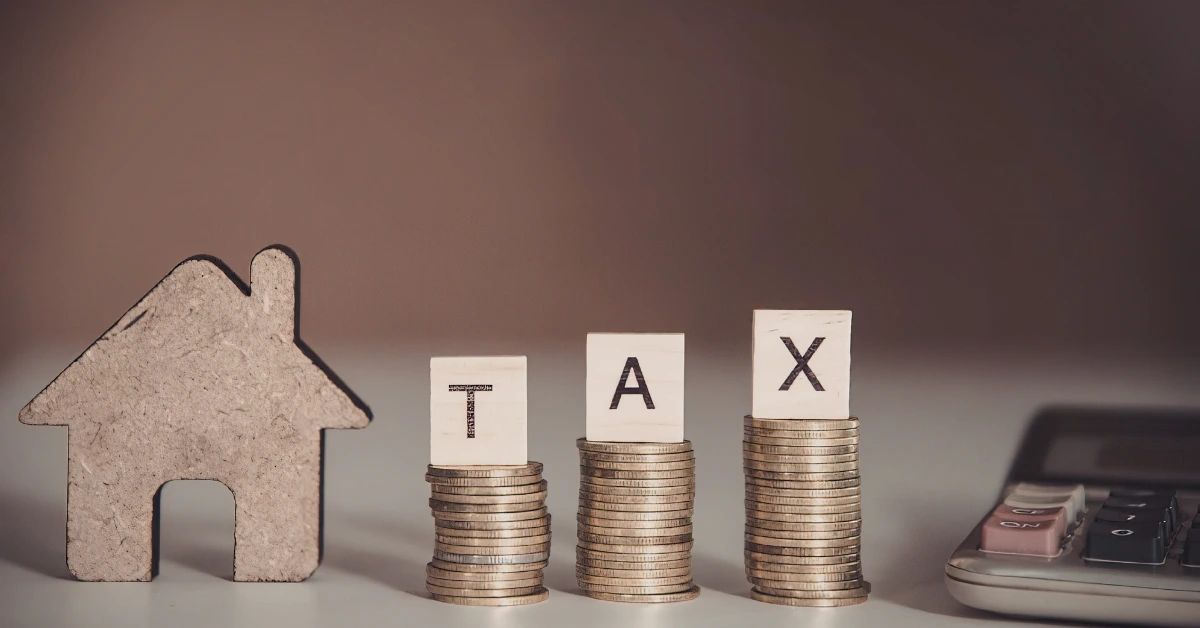 Stacks of coins labeled tax next to a house model and calculator representing IRS property seizure for unpaid taxes.