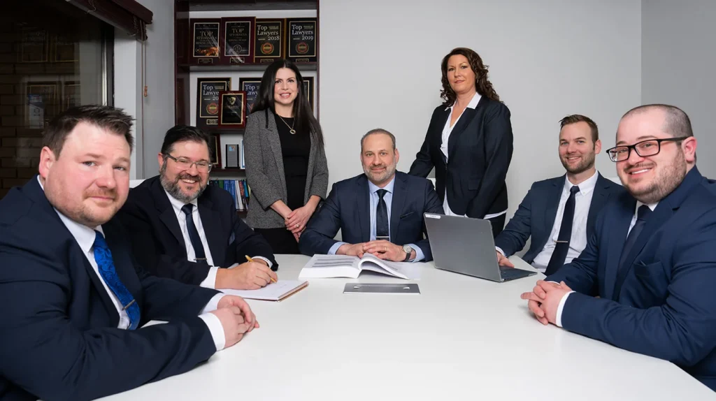 Professional legal team seated at a conference table in formal attire, smiling and ready to assist clients